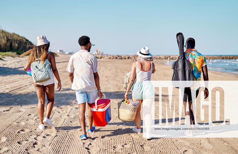 Full body back view of unrecognizable multiracial men and women in sunglasses and hat strolling on sand against cloudless blue sky while spending time on beach on summer day, Model released AdalbertoRodriguez_ID644_23524_006