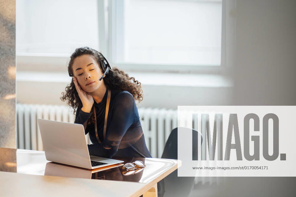 IMAGO Creative: Business, Innovative Technologie-Lösungen Young businesswoman wearing headset sitting with eyes closed at desk in office model released, Symbolfoto property released, JOSEF12858