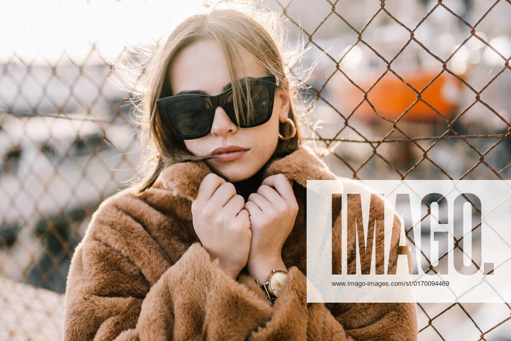 Young determined female in sunglasses and warm jacket standing near net fence and looking at camera CarlosRodelas_Tourist_9