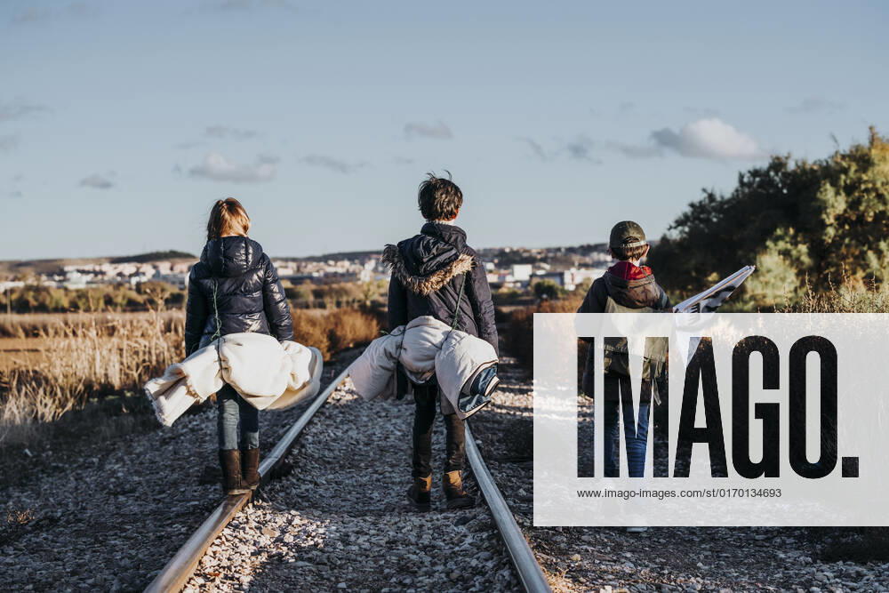 Back view of unrecognizable group of three children hiking in the woods walking in a train track, Model released JoseLuisCarrascosa_AdventureBoys_7