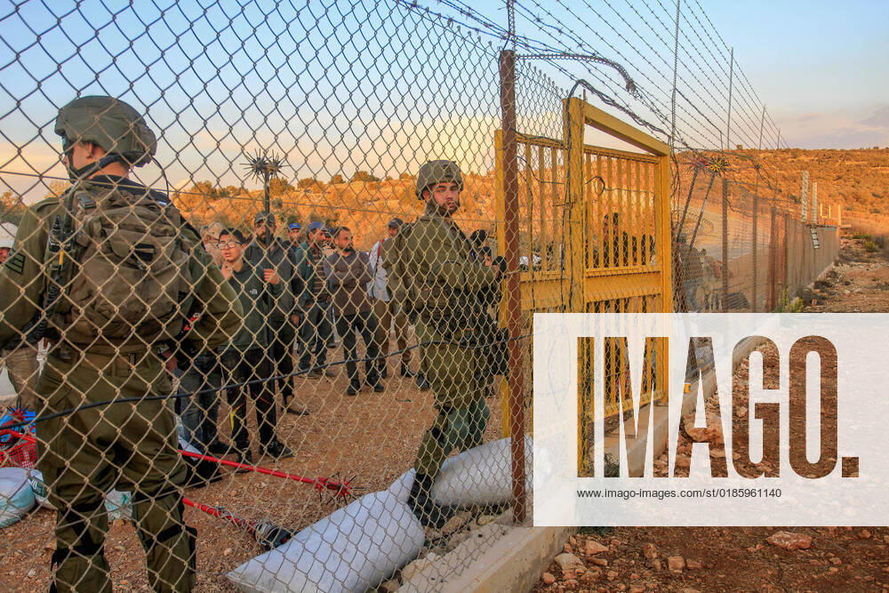 An Israeli soldier opens the gate of the separation barrier in the northern occupied West Bank for Palestinian farmers to enter their lands confiscated by Israel. Palestinian farmers closed the gates located on the wall separating the city of Salfit and the Jewish settlement of Ariel to reach their confiscated lands to pick olives, after the Israeli army opened them at seven in the morning and closed them until four in the evening and reopened them for the farmers to leave. Salfit Palestine - ZUMAs197 20221102_zaa_s197_137