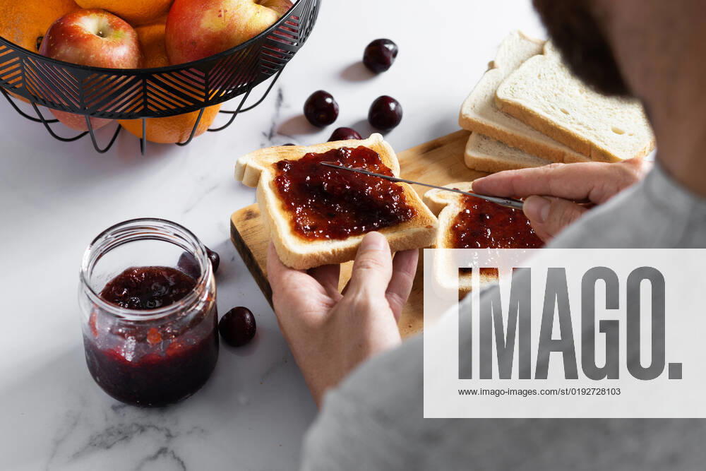 IMAGO Creative, Jahreszeit Sommer, Food, Marmelade kochen From above of crop anonymous man spreading sweet cherry jam on crispy toast with knife while preparing breakfast EstefaniaTorres_ID1062_40150_001