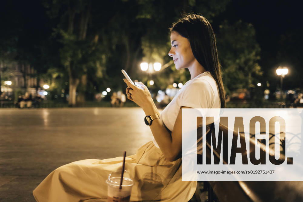 IMAGO Creative: Sommer, Sommertage im Stadtpark Woman using smart phone sitting on park bench at night model released, Symbolfoto, OYF00807