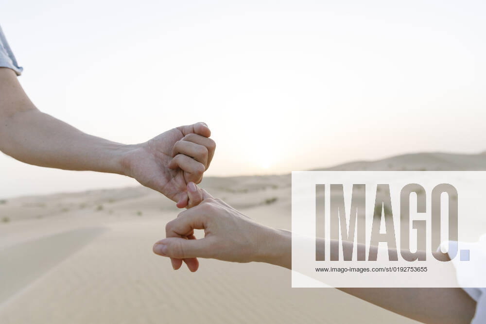 Hands of couple holding little fingers in desert at sunset model released, Symbolfoto, TYF00422