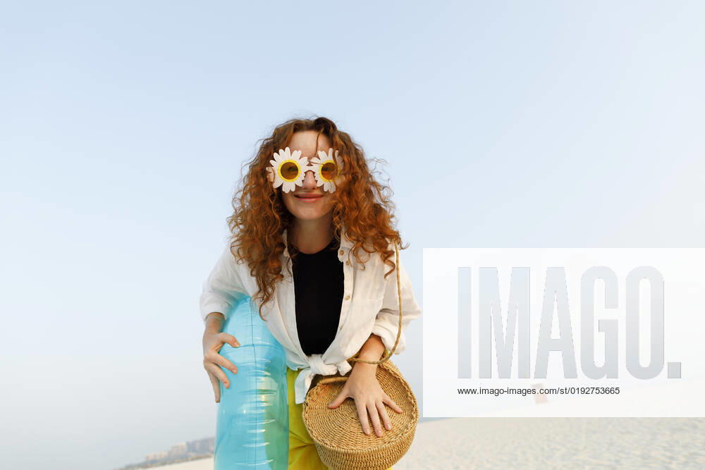 Smiling woman wearing sunflower sunglasses holding blue inflatable ring at beach model released, Symbolfoto, TYF00428