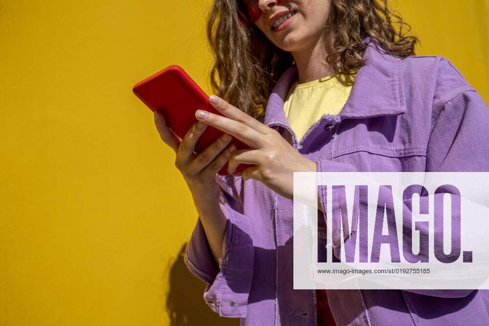 IMAGO Creative: Business, Innovative Technologie-Lösungen Woman wearing jacket using smart phone near yellow wall model released, Symbolfoto, VPIF07344