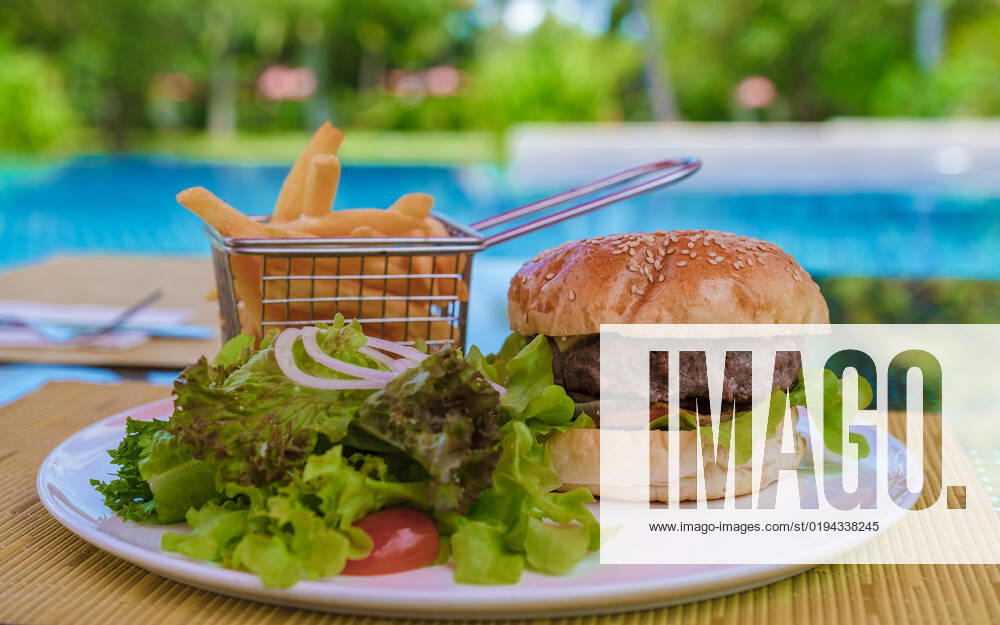 Hamburger with french fries on a plate isolated by a tropical pool Hamburger with french fries on a plate isolated by a tropical pool.