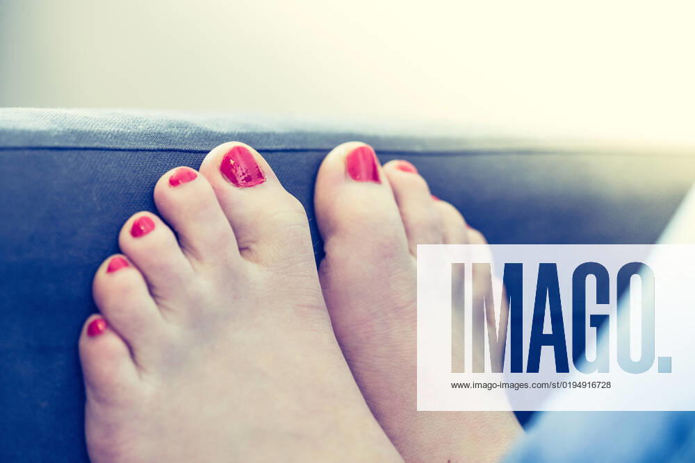 Female feet on a blue couch. Red nail polish, relaxing. Close up of female feet with red nail polish on a blue couch