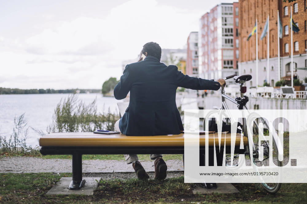 Rear view of businessman talking on smart phone while sitting near bay