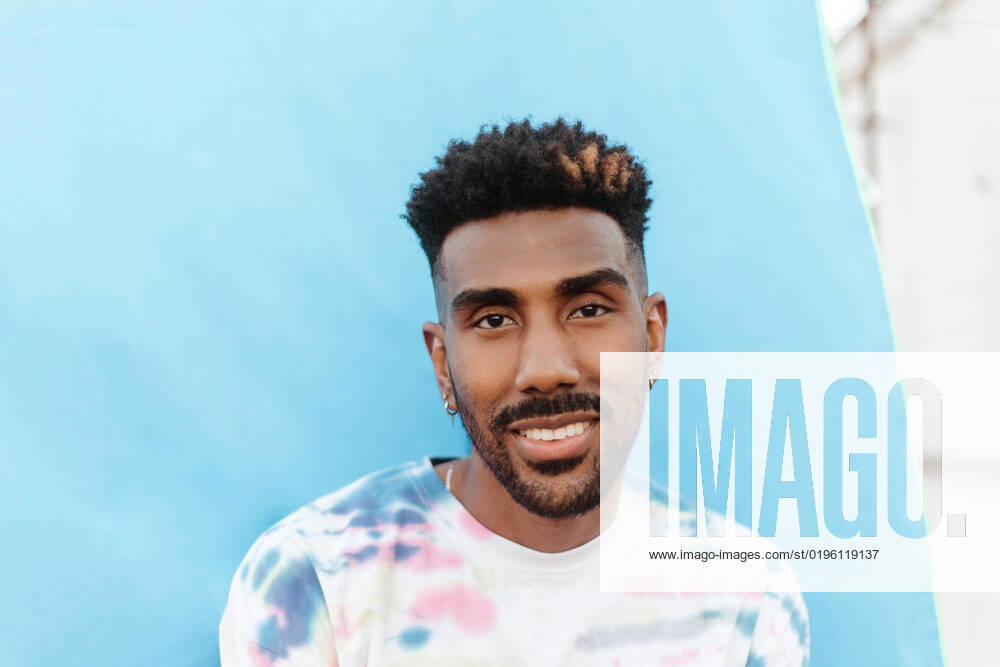 Portrait of positive black bearded male in t shirt with multicolored print and earrings having Afro haircut looking at camera and smiling, Model released AlbaCaro_ID3030_100314_028