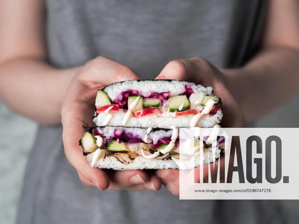 Vegan onigirazu in woman hands Vegan sushi sandwich onigirazu with mushrooms and vegetables.Healthy dinner recipe and idea. Colorful japan big roll sandwich onigirazu with red cabbage,radish,cucumber,mushrooms.Trend food.Copy space