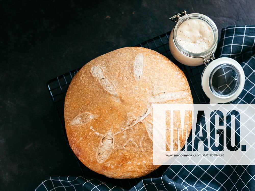 Wheat round sourdough bread, copy space, top view Wheat round sourdough bread and sourdoug starter in glass jar. Top view of delicious homemade sourdough bread on black background with copy space. Home made sourdough bread making concept.