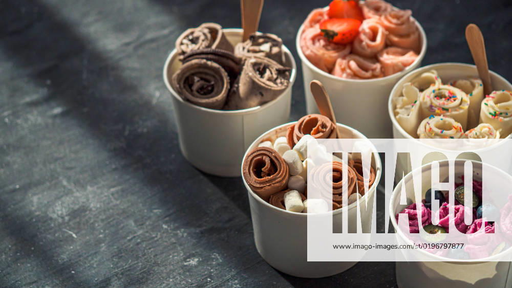 Rolled ice creams in cone cups on dark background Rolled ice cream in cone cups on dark background. Different iced rolls or Thai style rolled ice cream with copy space for text or design. Banner. Natural hard daylight