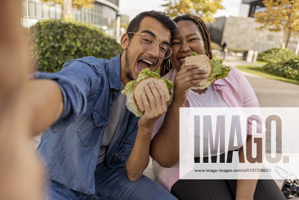 Happy young couple eating sandwich and taking selfie at footpath model released, Symbolfoto, JCCMF08076