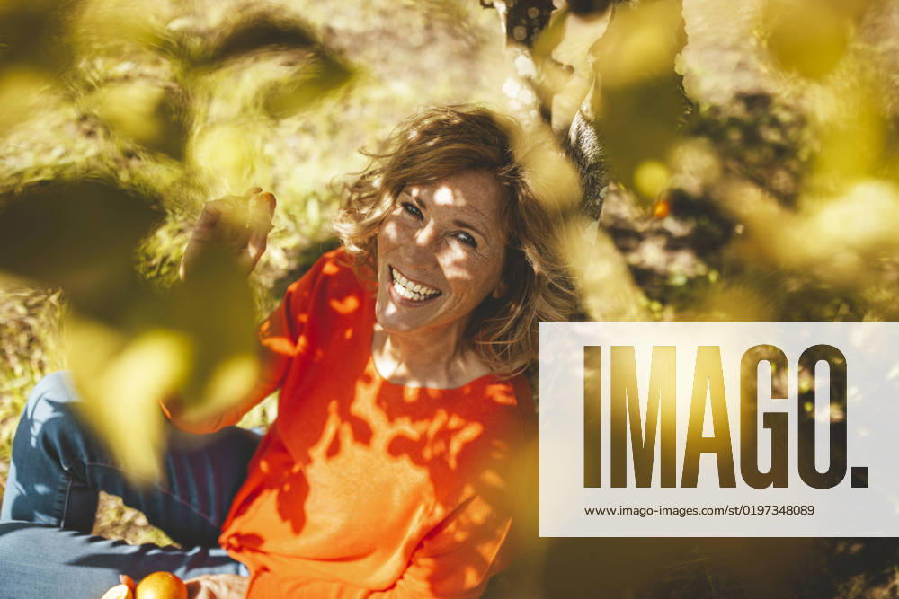 Happy mature woman sitting with orange fruits under tree model released, Symbolfoto property released, JOSEF15597