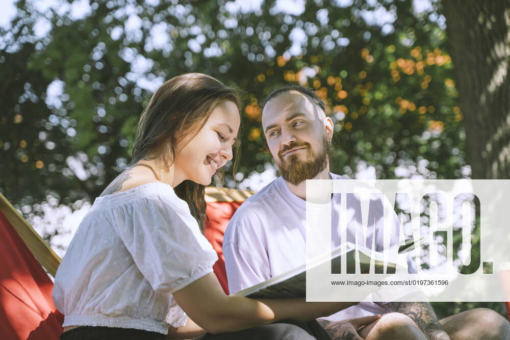 Hipster man looking at girlfriend smiling and reading book in backyard model released, Symbolfoto property released, NDEF00321