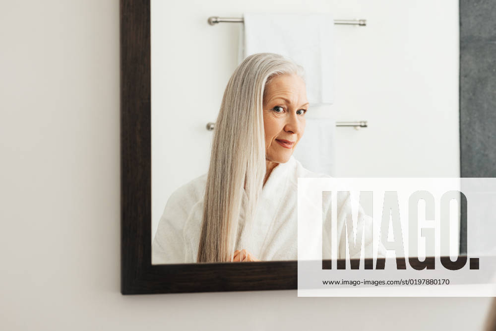 Portrait of an aged woman with long grey hair. Female looking in the mirror admires her hair. Portrait of an aged woman with long grey hair. Female looking in the mirror admires her hair.