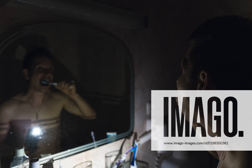 Power failure or blackout in the home. A young man brushes his teeth with a toothbrush in a dark bathroom and shines the flashlight in his smartphone. Energy crisis icon image