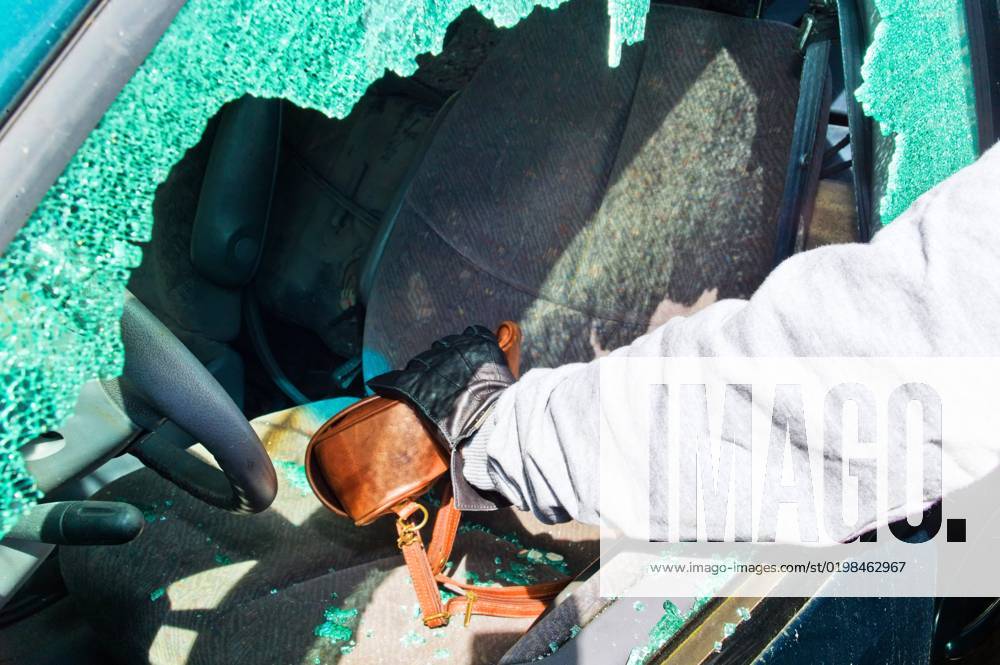 Thief steals a Handbag from the Car through a Eingeschlagene Disc Thief steals a handback from a Car Through a Broken Window Pane BLWS678346