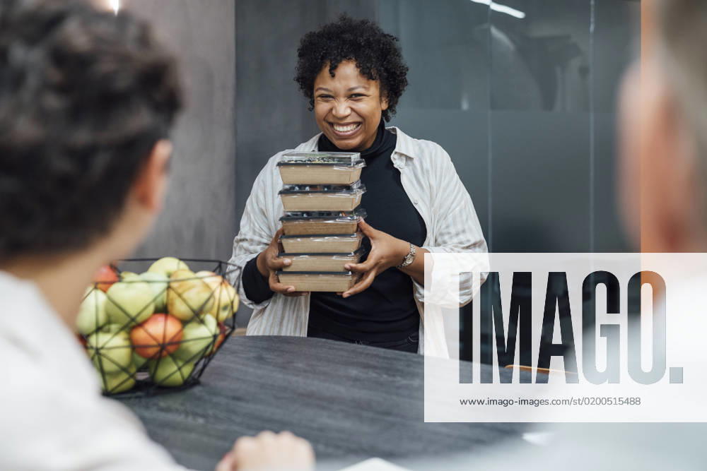 Cheerful young woman with lunch boxes standing by table in office model released, Symbolfoto property released, VPIF07749