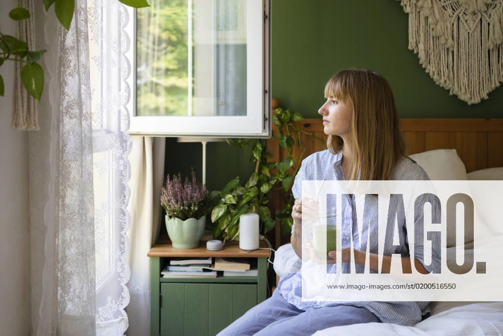 Thoughtful woman with smoothie sitting on bed at home model released, Symbolfoto property released, SVKF00955