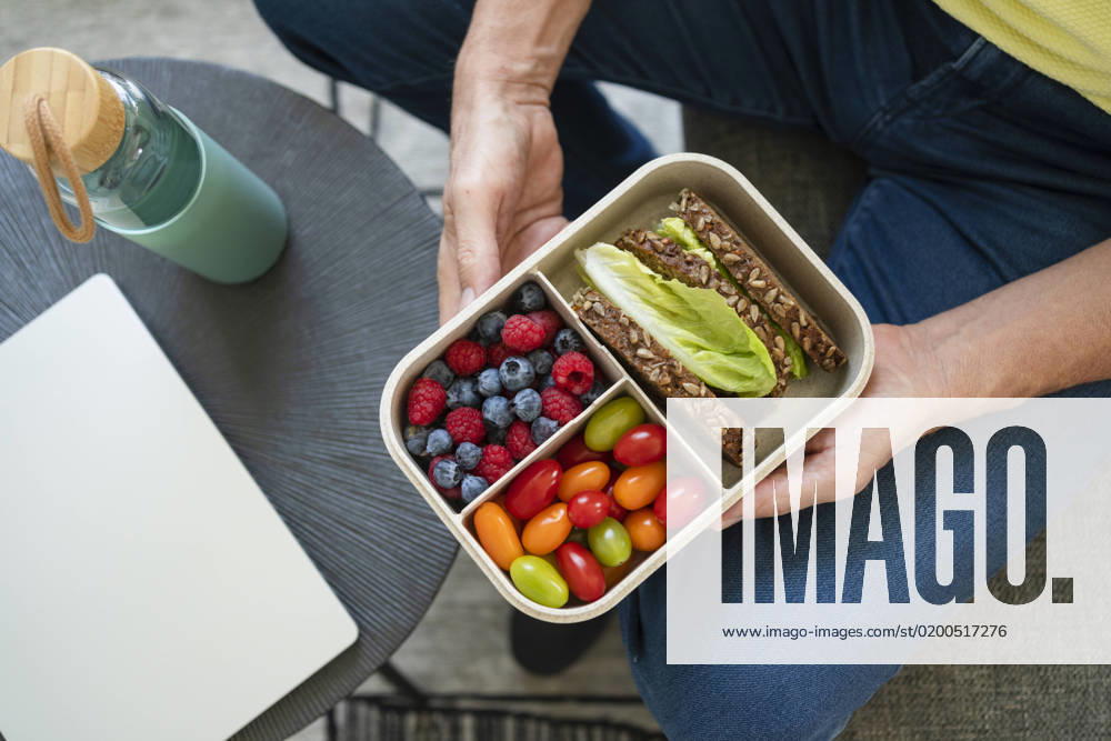 Hands of man holding lunch box with healthy food on sofa model released, Symbolfoto property released, SVKF01015