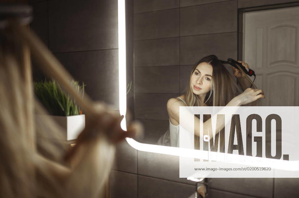 Woman curling hair with tongs in front of mirror at home model released, Symbolfoto property released, ANAF00800