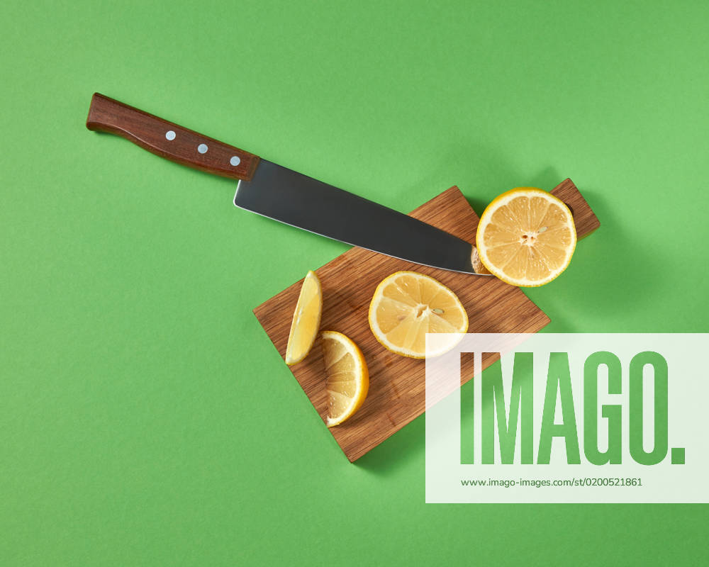 Half and slices of fresh tropical yellow lemon on a wooden cutting brown board with a steel knife. View from above. Top view of halfs and slices of natural lemon on a cutting wooden board. A sharp steel knife is cut by organic citrus fruit.