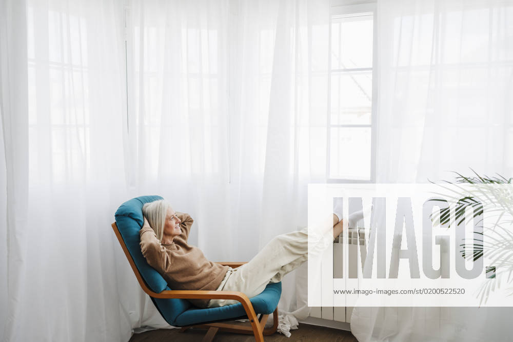 Woman relaxing on armchair in front of window at home model released, Symbolfoto property released, EBBF07681