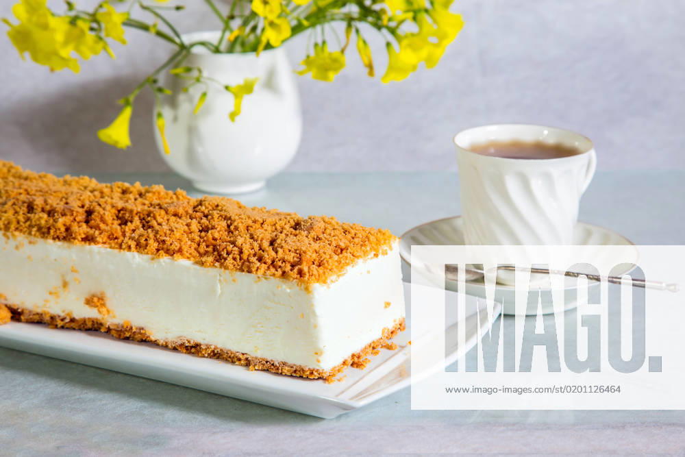 White cheesecake Gorgeous white cheesecake, sprinkled with sweet crumbs. Professional bakery. The background is porcelain cup with hot tea and vase with daisies