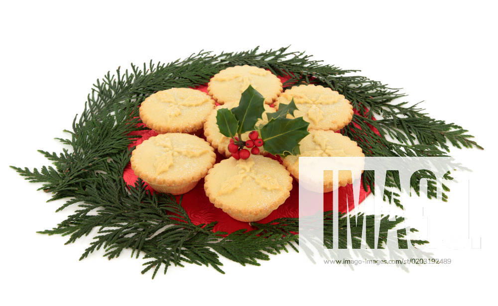 Christmas mince pie group with holly and red berry leaf sprig surrounded by cedar leaf sprigs over white background.
