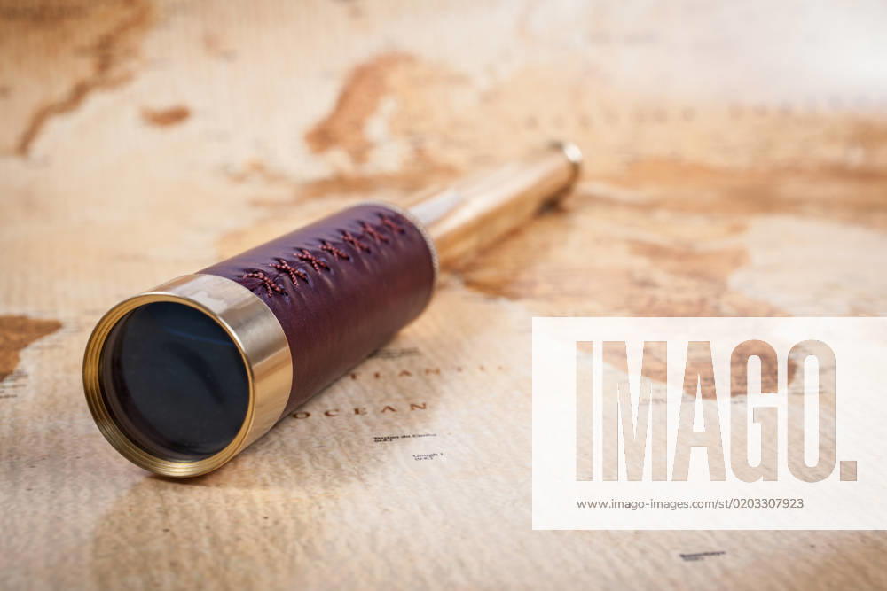 An antique, out of focus, map with a beautiful golden and leather telescope.