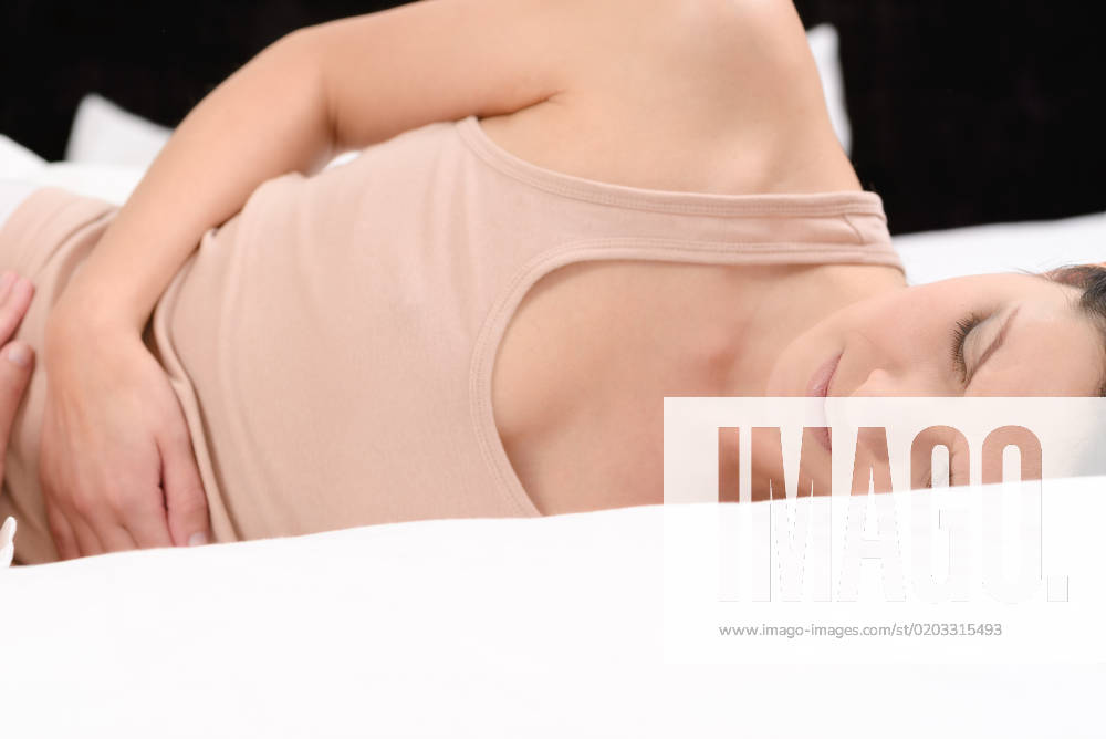 Frau mit akuten Bauchschmerzen Woman with her monthly menstrual pains clutching her stomach with her hands as she becomes stressed by the ongoing cramps while sitting in her bed