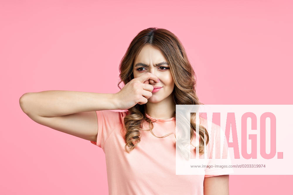 Smells bad, woman pinching nose with disgust on pink background Smells bad, woman pinching nose with disgust on pink background. face expression concept