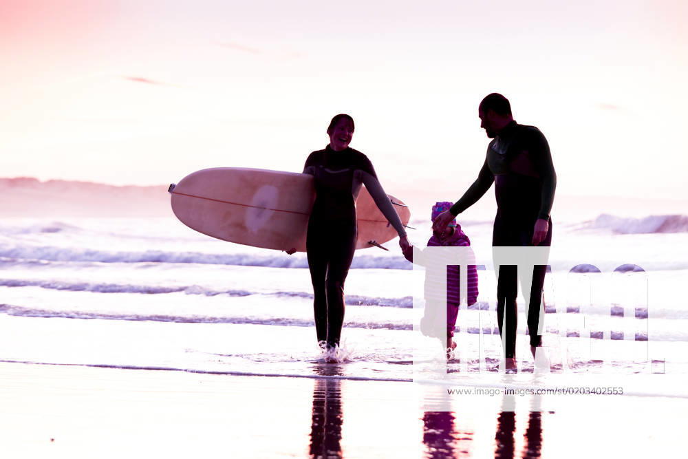 Female surfer and her familly walking in the beach at the sunset