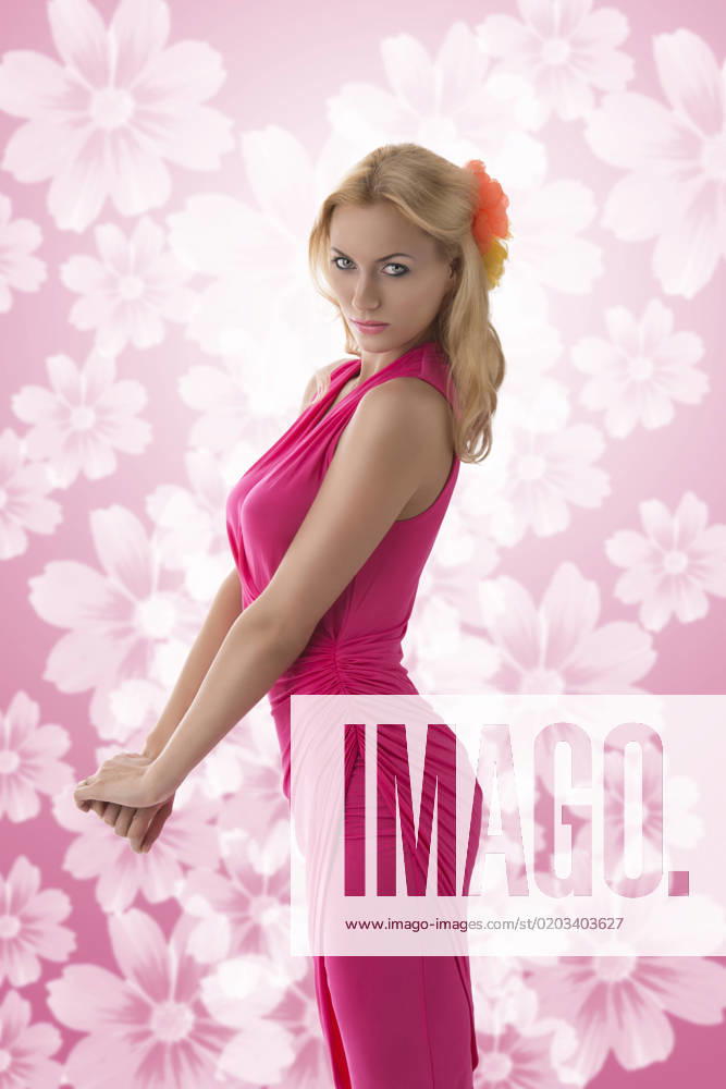 IMAGO Creative, Lifestyle, Barbiecore pretty blonde girl with pink dress and flowers in the hair, her body is in profile and she looks in to the lens