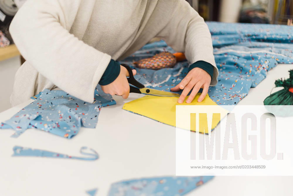 Unrecognizable female tailor in casual sweater cutting piece of colorful fabric with scissors while working on project in creative atelier, Model released, Property released AlbaCaro_ID12631_384004_048