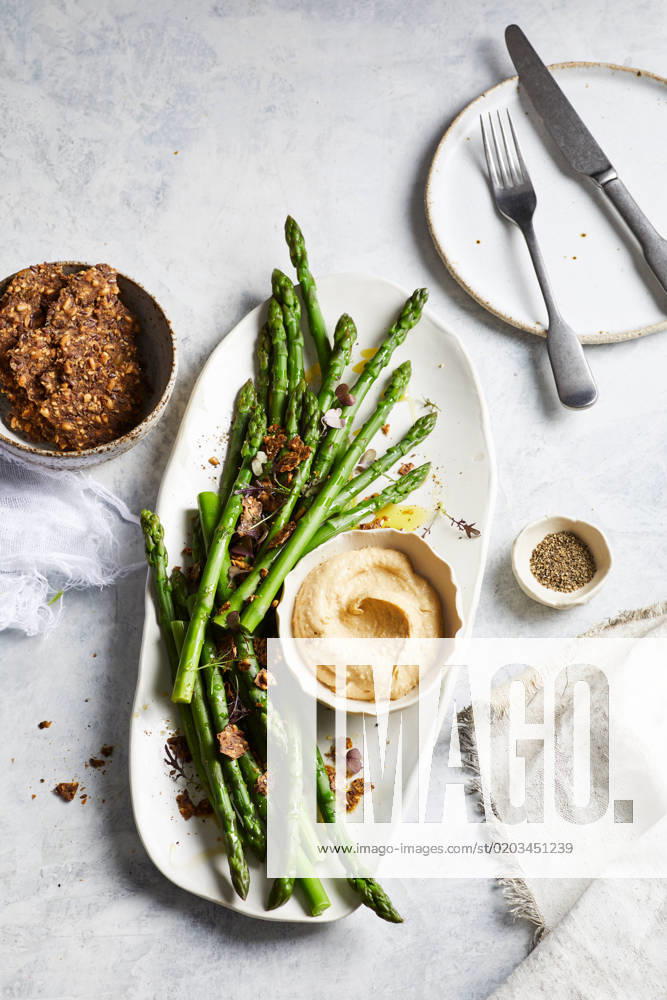 Top view of yummy hummus with asparagus served on white plate near bowl of crispy seed crackers on marble table in kitchen GeorgiaGold_ID12873_391218_001