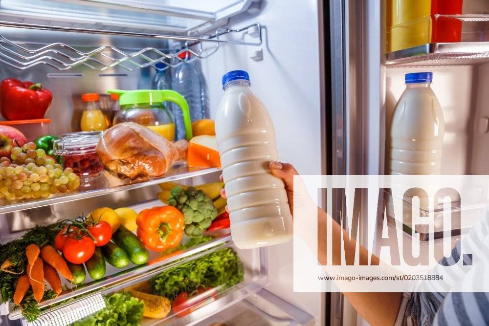 Woman takes the milk from the open refrigerator