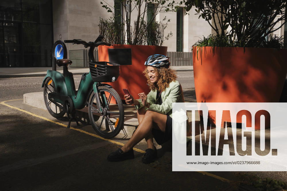 Businesswoman surfing net through smart phone sitting by electric bicycle model released, Symbolfoto, PWF00643
