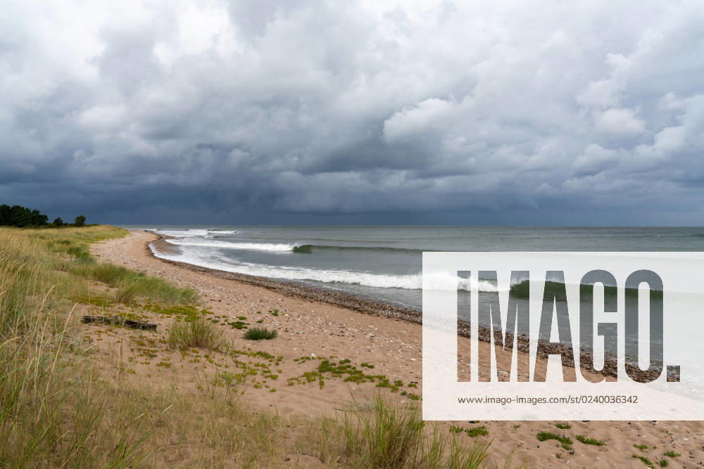Sets of neat waves breaking on a sandy beach with marsh grass and sand dunes and a dark ominous sky overhead Sets of neat waves breaking on a sandy beach with marsh grass and sand dunes and a dark ominous sky overhead
