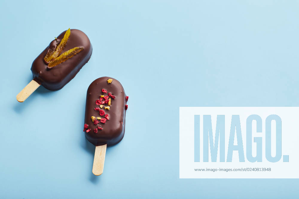 Mousse dessert with fruit flavors in the form of popsicle ice cream on blue background. Mousse dessert with fruit flavors in the form of popsicle ice cream covered with dark chocolate on blue background.