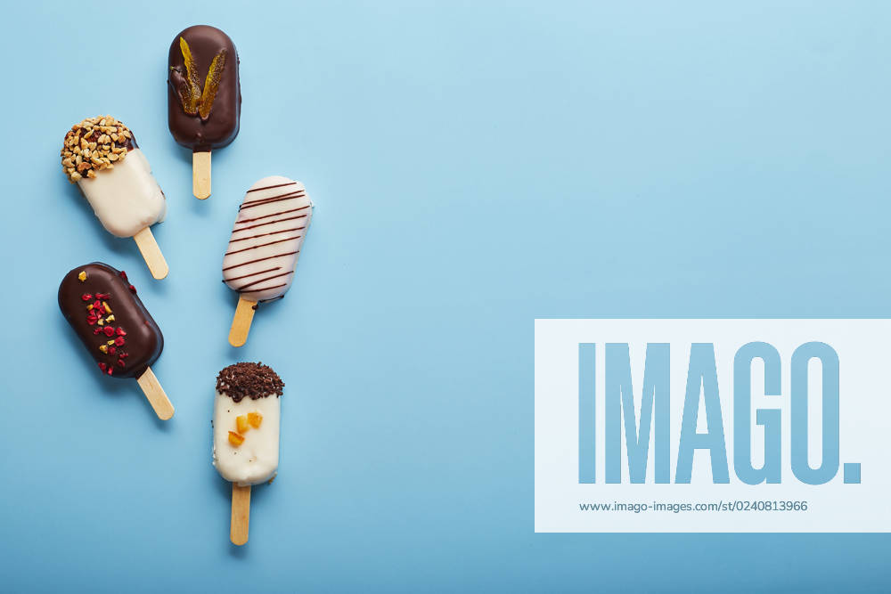 Mousse dessert with fruit flavors in the form of popsicle ice cream on blue background. Mousse dessert with fruit flavors in the form of popsicle ice cream covered with white and dark chocolate on a blue background.