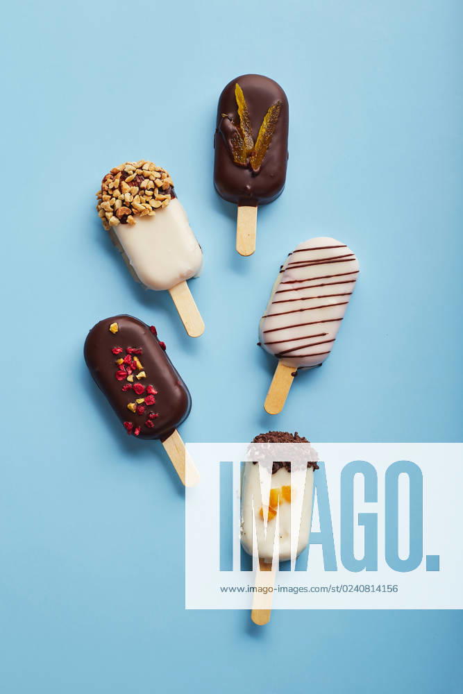 Mousse dessert with fruit flavors in the form of popsicle ice cream on blue background. Mousse dessert with fruit flavors in the form of popsicle ice cream covered with white and dark chocolate on a blue background.
