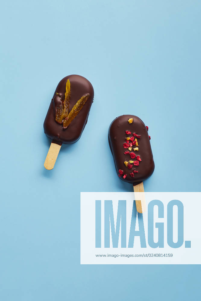 Mousse dessert with fruit flavors in the form of popsicle ice cream on blue background. Mousse dessert with fruit flavors in the form of popsicle ice cream covered with dark chocolate on blue background.