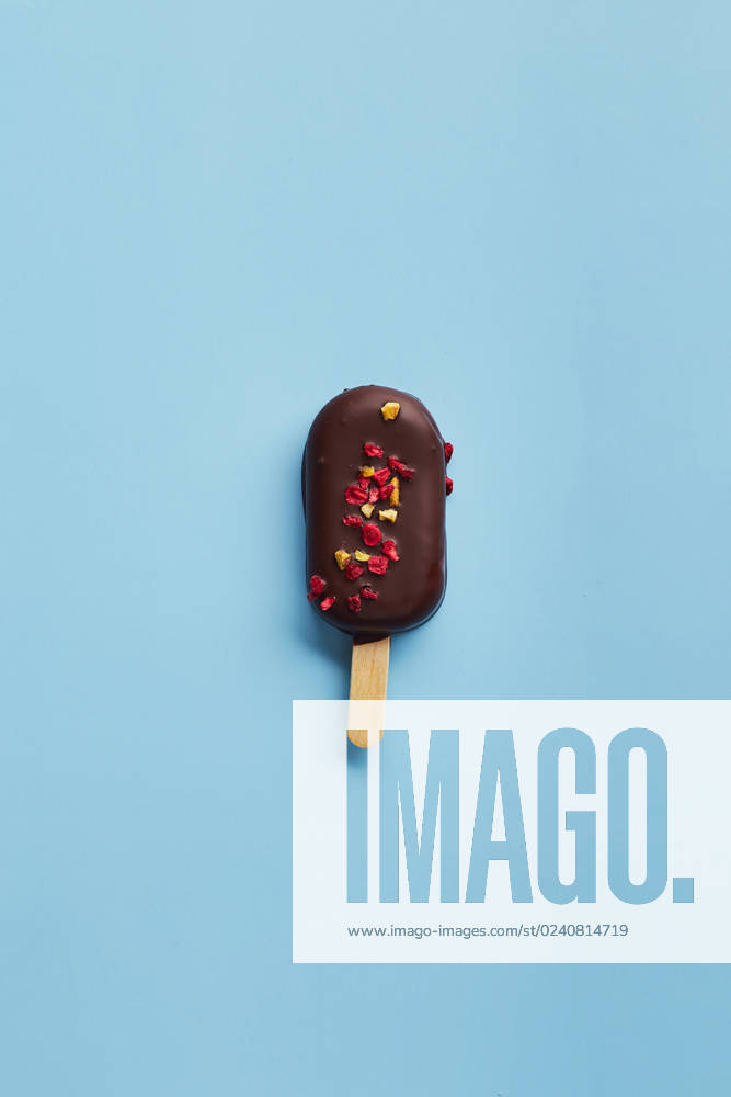 Mousse dessert with fruit flavors in the form of popsicle ice cream on blue background. Mousse dessert with fruit flavors in the form of popsicle ice cream covered with dark chocolate on blue background.