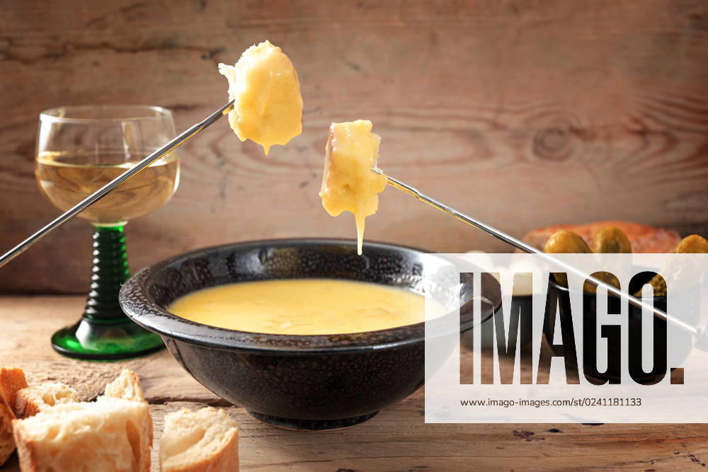 Swiss fondue from melted cheese with bread on long forks, pickles and wine on rustic wooden planks, copy space, selected focus Swiss fondue from melted cheese with bread on long forks, pickles and wine on rustic wooden planks, copy space, selected focus, narrow depth of field