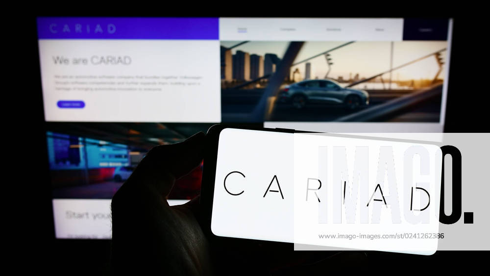 Person holding cellphone with logo of German automotive software company Cariad SE on screen. Stuttgart, Germany - 10-15-2022: Person holding cellphone with logo of German automotive software company Cariad SE on screen in front of business webpage. Focus on phone display.