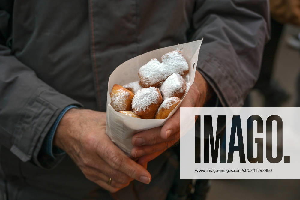 Man holding a paper bag of Mutzenmandeln, deep fried shortcrust dough pastry with almonds covered with powdered sugar, traditional German fair snack on Christmas, New Year and Carnival, copy space Man holding a paper bag of Mutzenmandeln, deep fried shortcrust dough pastry with almonds covered with powdered sugar, traditional German fair snack on Christmas, New Year and Carnival, copy space