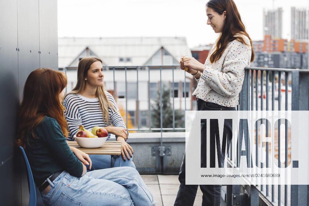 IMAGO Creative, Lifestyle, Leben in einer Wohngemeinschaft, WG Group of friends, college students on a balcony of their dorm room Young caucasian woman college students, sitting on the rood top of their dorm room, eating a snack taking a break from studying, getting some fresh air, on a cloudy autumn day. ,model released, Symbolfoto